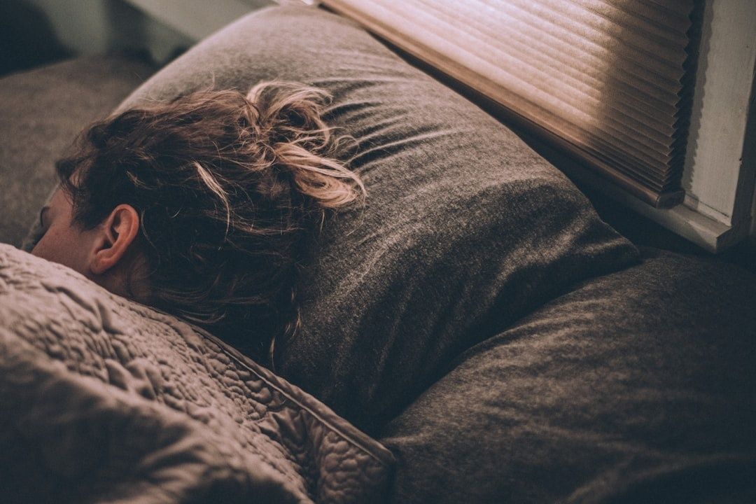 Person sover på sidan under ett täcke i ett mörkt sovrum